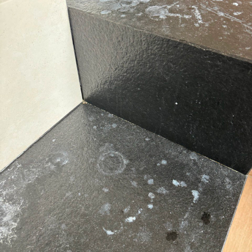 alt="Czarna powierzchnia z białymi plamami w rogu ściany"