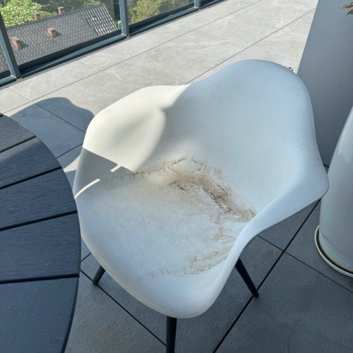 alt="Biały plastikowy krzesło z zabrudzeniami na tarasie"